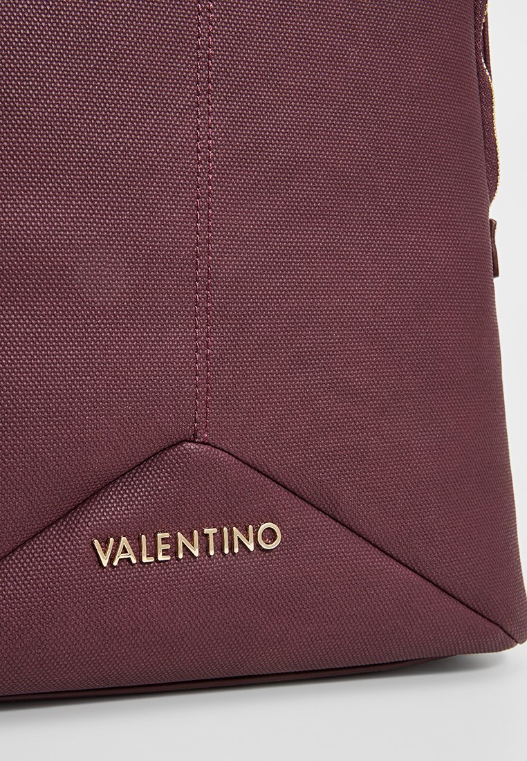 Burgunderfarget teksturert veske med en trekantet bunn, med gullpræget logo "VALENTINO" og kontrasterende sømdetaljer.