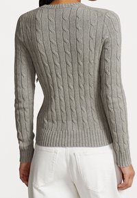 Femme portant un pull gris ajusté en tricot torsadé et un pantalon blanc, vue de dos.