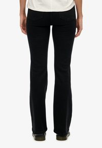 Pantalones vaqueros negros acampanados con una textura suave, que presentan bolsillos traseros estándar y una cintura ajustada, que se extienden hasta un dobladillo acampanado en los tobillos.