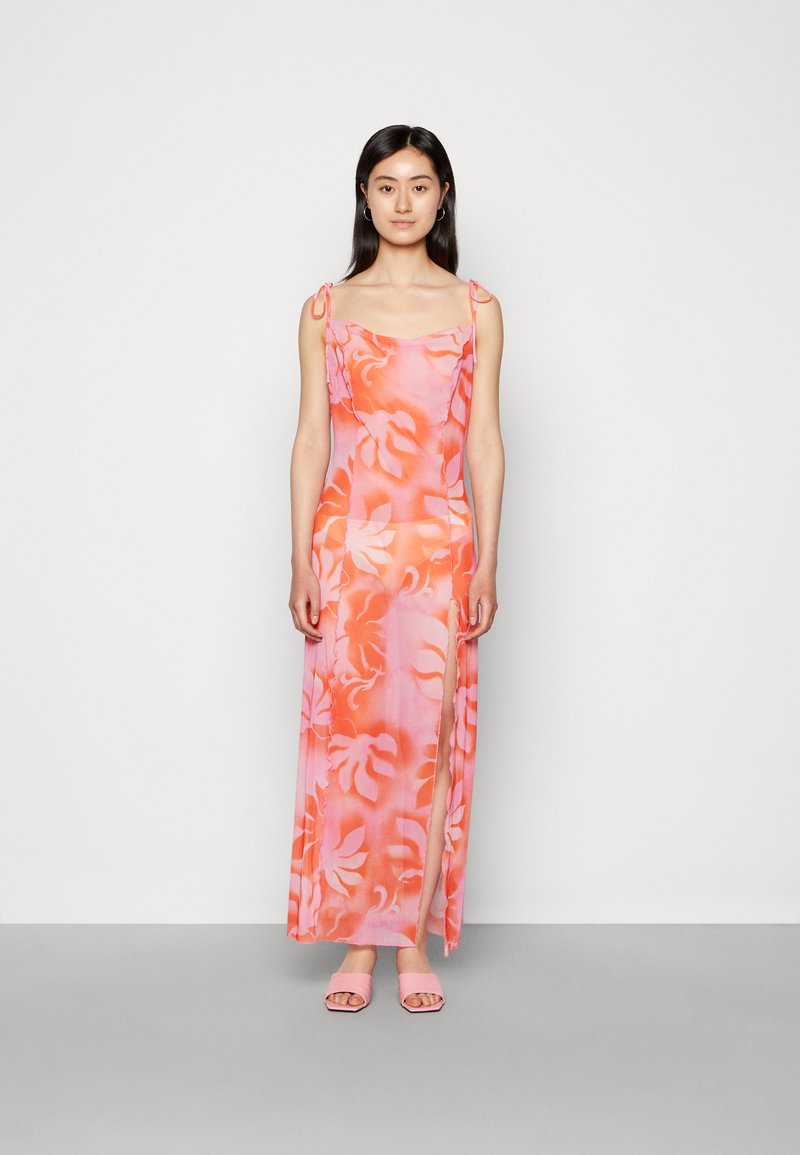 Vestido maxi floral rosa com alças finas e fenda lateral, apresentando um design em degradê. Acompanhado de sandálias rosa de salto bloco.