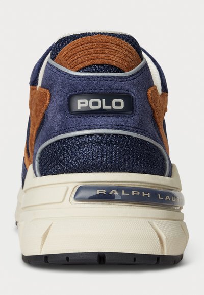 Zapatillas navy y marrones con materiales de ante y malla, que presentan una gruesa suela color crema, una marca prominente en el talón y acentos texturizados.