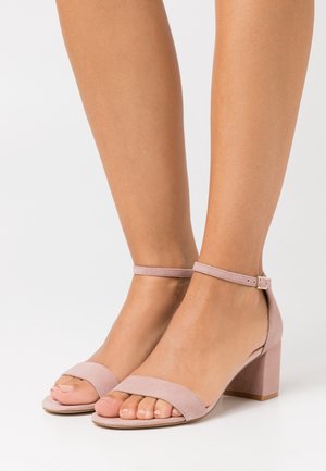 Sandales à talons en daim rose clair avec talon bloc, design à bout ouvert et fine bride à la cheville ornée d'une boucle dorée.