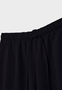 Pantalon avec taille élastique noire muni d'un cordon de serrage noué à l'avant, tissu lisse, sans motifs ni logos visibles.