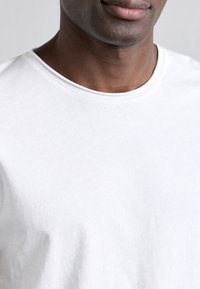 Biely bavlnený tričko s okrúhlym výstrihom, hladkou textúrou a krátkymi rukávmi. Tkanina pôsobí ľahko a jemne. Minimálne dizajnové detaily.