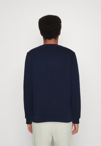 Felpa blu navy con collo a giro, maniche lunghe e polsini a coste. Texture liscia, design minimale e silhouette aderente.
