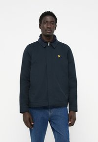 Navy blue jacket with a collar, zip closure, and side pockets. Yellow logo on chest. Made from a smooth, durable fabric.