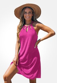 Robe sans manches fuchsia avec un décolleté en forme de clé, un design fluide et une texture douce. Portée avec un chapeau en paille à large bord.
