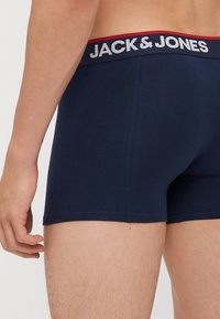 Mörkblå boxershorts med en röd och vit elastisk midja som pryder "JACK & JONES"-logotypen, slät textur och kroppsnära passform.