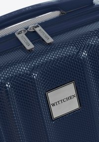Navyblauwe harde koffer met een honingraatachtig patroon, dubbele zilveren ritssluitingen en een metalen logo plaat met de tekst "WITTCHEN."