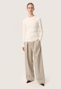 Ribbed cream knit top with a crew neck, paired with wide-leg beige trousers and pointed black heels, highlighting a relaxed fit.