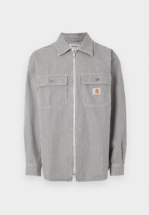 Langärmliges graues und weißes Hemd mit vertikalen Streifen, Reißverschluss, zwei aufgesetzten Taschen vorne, einem Kragen und einem kleinen orangefarbenen Logopatch auf der rechten Tasche.