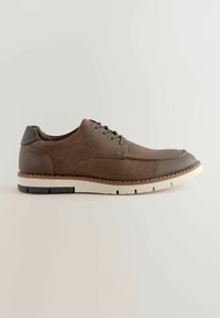 Zapato de cuero marrón con un upper texturizado, diseño de cordones y suela blanca contrastante. Presenta una costura adornada y un acento en el talón de goma.