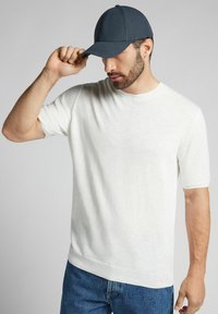 Lichtgewicht, kortekorte witte sweater met een ronde hals, gecombineerd met een donkerblauwe baseballpet met een gestructureerd ontwerp.