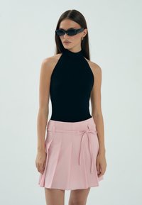 Czarny bodysuit na ramiączkach połączony z jasnoróżową plisowaną spódnicą z bocznym wiązaniem, prezentowany na neutralnym tle.