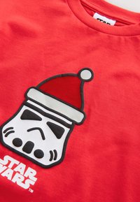 Indumento rosso con un elmo di Stormtrooper bianco e nero che indossa un cappello di Babbo Natale rosso, con il logo "Star Wars" sotto.