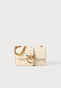 Cream leather handbag with gold chain strap, featuring a circular hardware accent with two bird figures and decorative studs on the front.