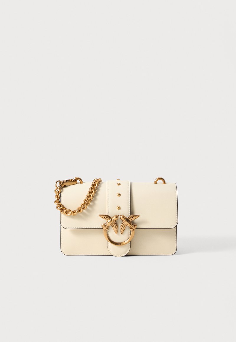 Cream leather handbag with gold chain strap, featuring a circular hardware accent with two bird figures and decorative studs on the front.