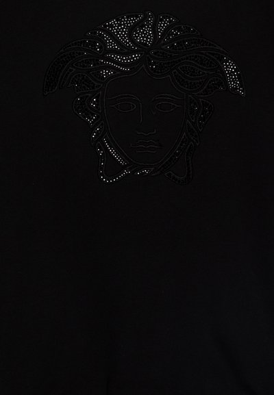 Black garment featuring a textured design of a face with flowing hair, adorned with shiny studs. Smooth fabric with an even surface.