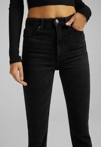 Jeans ajustados de tiro alto en negro, hechos de denim, con una silueta ajustada, cinco bolsillos y un cierre de botón plateado en la cintura.