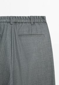 Zbliżenie na szare spodnie z elastycznym pasem, szlufkami na pasek i pojedynczą kieszenią z klapką po prawej stronie z tyłu.