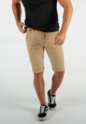 Shorts kaki avec ourlets roulés, fabriqués en tissu léger. Associés à un t-shirt noir ajusté et des baskets noires avec des accents blancs.