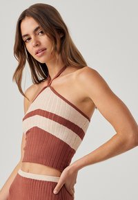 Top cropped a maglia in ruggine e beige, con texture a coste, design asimmetrico e collo halter. Le righe orizzontali aggiungono interesse visivo.