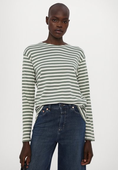 Langermet, grønn og hvit stripet T-skjorte laget av mykt stoff, kombinert med mørkeblå jeans. Har en avslappet passform og båtnekk.