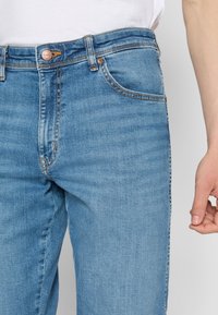 Ljusblå denimjeans med rak passform, femfickorsdesign, synlig sömnad och kopparnitdetalj vid midjebandet.