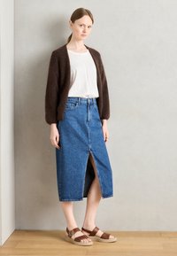 Brown fuzzy cardigan, white t-shirt, blue denim skirt with front slit, brown sandals with a strap, and round hardware detail.