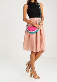 Różowa plisowana spódnica połączona z czarną prążkowaną bluzką na ramiączkach oraz torebką na ramię w motyw arbuza, z akcentami w kolorze teal i czarnymi pestkami.