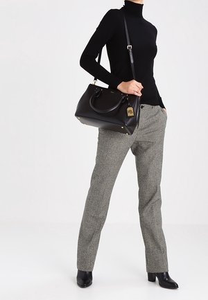 Frau trägt schwarzen Rollkragenpullover, karierte Hose, schwarze Stiefeletten, hält schwarze Lederhandtasche mit goldenem RL-Logo-Tag.
