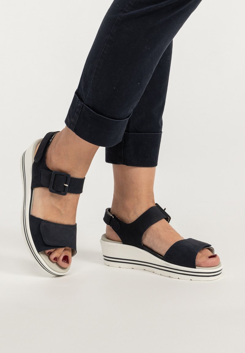 Dunkelblaue Keilsandalen mit verstellbaren Riemen, einer Schnallenakzentuierung und einer weiß gestreiften Sohle; weiches, strukturiertes Material, offene Zehen.