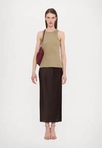 Khaki rebrast top z ribami, v kombinaciji z rjavim plisiranim maxi krilom. Model drži bordo torbico in nosi bež sandale z trakci.