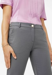 Pantaloni grigi realizzati in morbido tessuto con un design elegante, dotati di una tasca frontale, cuciture sottili e un dettaglio di bottone metallico circolare.