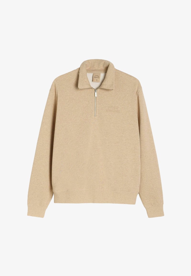 Beżowa bluza na zamek z wysokim kołnierzem, miękka w dotyku, z prążkowanymi mankietami i dołem. Posiada subtelne logo na klatce piersiowej w dopasowanym odcieniu.