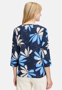 Marinebluse med trekvartærmer, prydet med et blomstermotiv i lys blå og creme. Blødt stof med en afslappet pasform og bred halsudskæring.