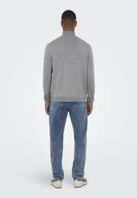 Pulover gri, cu mâneci lungi și guler înalt, asortat cu blugi din denim albastru deschis și adidași albi. Design simplu și casual.