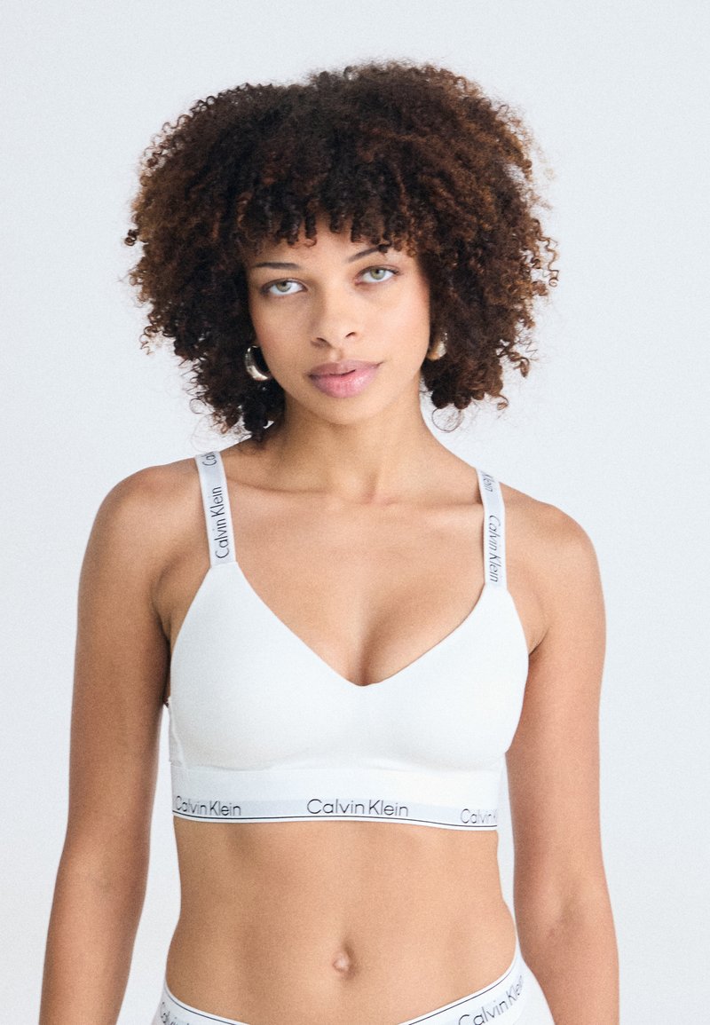 Witte bralette met een V-halsontwerp, zachte stof en Calvin Klein-logo op de elastische band en schouderbanden. Soepele textuur, sportieve pasvorm.