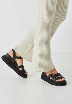 Sandalias plataforma negras con tiras cruzadas anchas y hebilla ajustable, con suela texturizada y acabado en cuero liso.