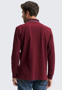 Langärmliges Polohemd in Bordeauxrot mit einem kontrastierenden Kragenband und einem weichen, strukturierten Stoff. Lässige Passform mit seitlichen Schlitzen.