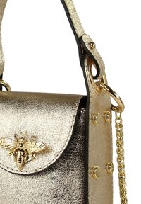 Goldfarbene metallische Handtasche mit einem Bienenförmigen Verschluss, ausgestattet mit einer Kettenriemen und gepunkteten Akzenten an den Seiten. Glatte Textur mit glänzendem Finish.