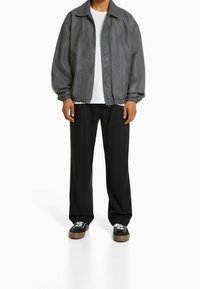 Szara kurtka bombowiec z elastycznymi mankietami, z kołnierzem, noszona na biał�ą koszulkę i czarne spodnie. Model stoi na jednolitym tle.