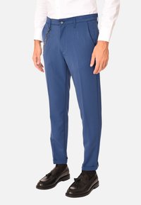 Pantaloni su misura blu realizzati in tessuto liscio, con una vita decorata da una catena argentata e un taglio dritto.