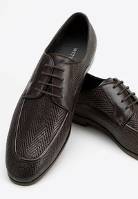 Scarpe da uomo marroni in pelle con un motivo a trama intrecciata, dotate di lacci e una sezione laterale liscia.