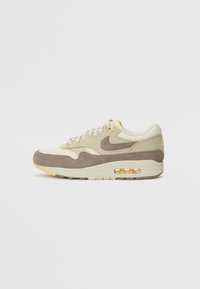 Μπέζ σουέτ και υφασμάτινο αθλητικό παπούτσι, με καφέ λογότυπο σούσι, κίτρινες λεπτομέρειες και διαφανή αέρινη σόλα. Σχεδιασμένο με στρογγυλή μύτη και υφή στην σόλα.