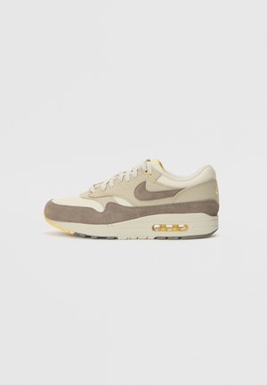 Beige zamšs un tekstila sneakers, ar brūnu zvīņu, dzelteniem akcentiem un caurspīdīgu gaisa spilvenu. Izstrādāta ar noapaļotu purngalu un teksturētu zoli.
