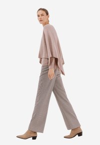 Světle růžový oversized pletený svetr s vrstveným designem, v kombinaci s vysokým pasem, kostkovanými širokými kalhotami a taupe kotníkovými botami.