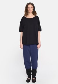 Czarny oversize t-shirt z krótkim rękawem, w połączeniu z granatowymi spodniami dresowymi i czarnymi rozgrzewaczami nóg; noszony z czarnymi baletkami.