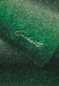 Zelena teksturirana deka s gradijentnim dizajnom. Sadrži svijetlozelene do tamnozelene nijanse te izvezeni "Carhartt" logo u bijelom koncu.