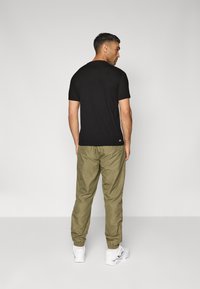 Svart kortermet t-skjorte, avslappet passform, kombinert med olivengrønne joggebukser, elastiske mansjetter. Modellen står med ryggen mot kameraet, hvite sneakers synlige.